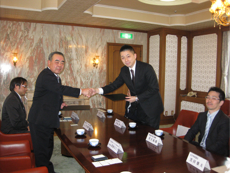 菅義雄会長と固く握手をかわす古本泰之委員長
