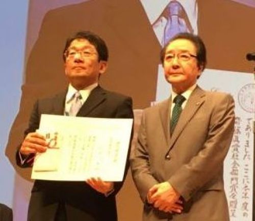 左：竹内名誉学長・名誉教授への賞状を掲げる塩川教授